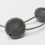Close-up of a metal coin necklace: round discs threaded on a twisted wire chain, with an eagle design visible on the front.